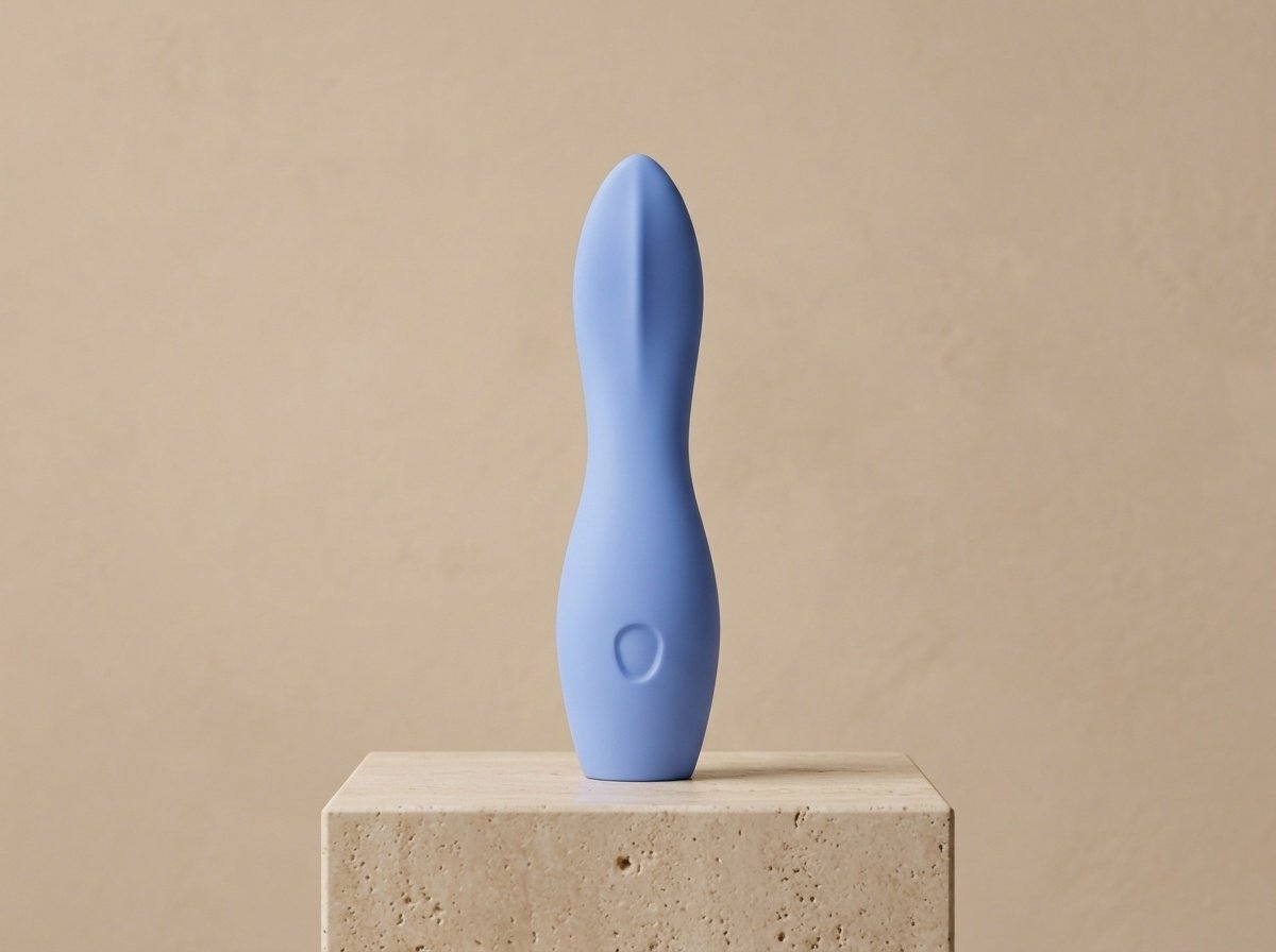 Clean studio photograph of the periwinkle Dame Dip vibrator standing elegantly on a travertine pedestal showcasing its balanced hourglass waist and tapered scoop tip
