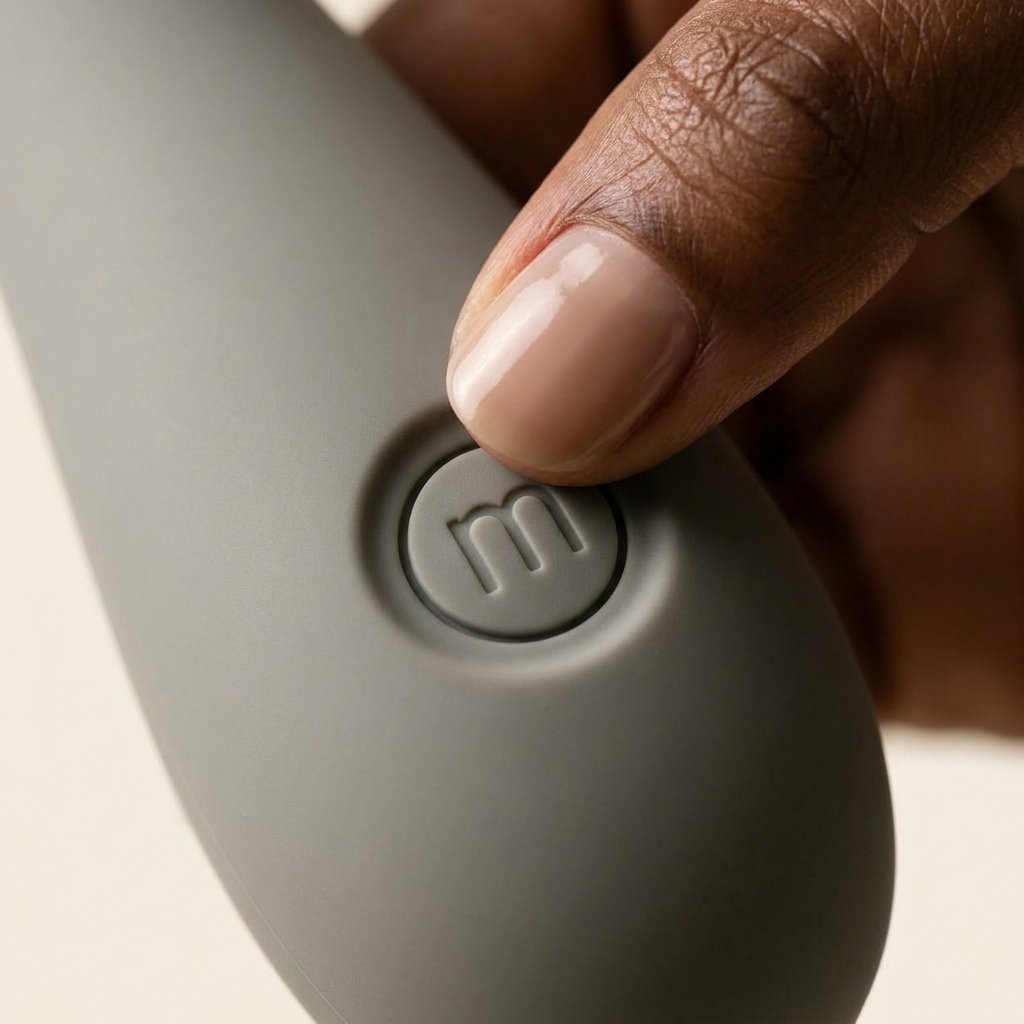 Macro photograph showing a thumb pressing the flush circular silicone control button on the Maude Spot handle with its debossed 'm' monogram