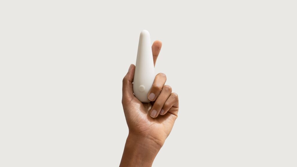 Authentic photograph of the Maude Vibe personal massager held pen-style in hand against a neutral studio background