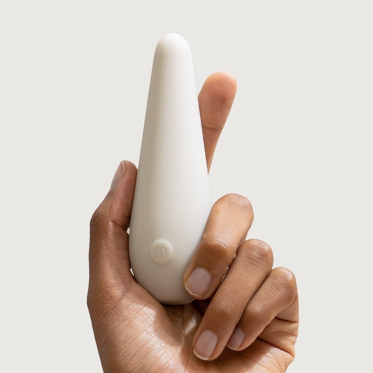 Detailed close-up view of the Maude Vibe vibrator held between fingers, showing the indented power button and tapered tip
